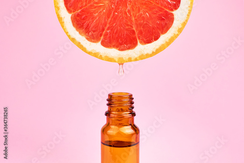 Fotografiet Citrus oil drop dripping from grapefruit slice into dark glass bottle