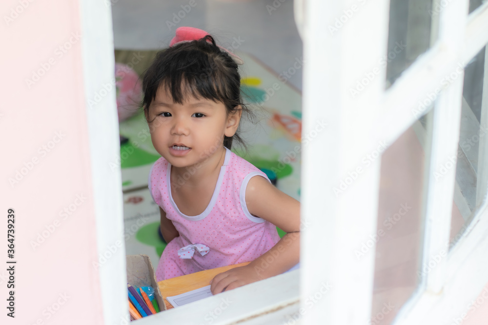 An 2-3 year-old Asian girl sitting on a window writing practice and looking out the window An 2-3 year-old Asian girl sitting on a window writing practice and looking out the window