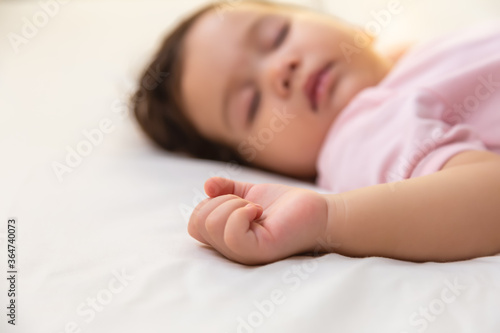 Adorable innocent little girl sleeping on bed with good dream. Cute mixed race infant baby feel comfortable and taking a rest, relaxed and peaceful. Lovely toddler girl wear pink baby dress focus hand