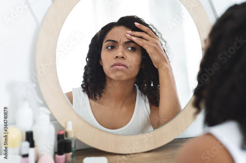 Fine lines and wrinkles. Concerned black woman checking aging signs on face photo