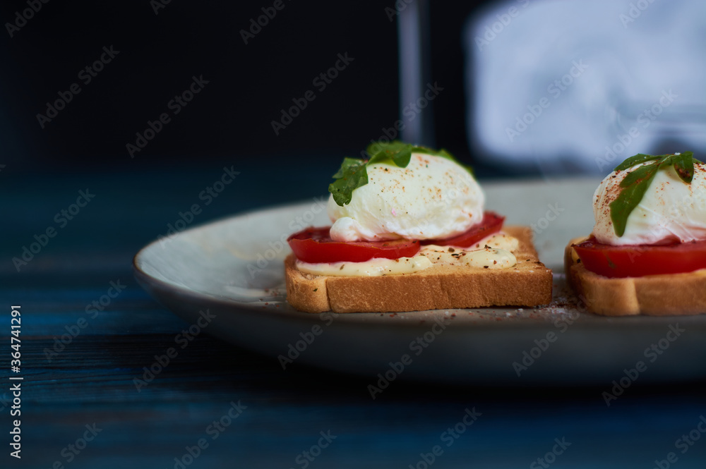 Large gray ceramic plate with toast and poached eggs, greens, tomatoes, sauce. Tasty breakfast. Glasses of wine. Large gray ceramic plate with toast and poached eggs, greens, tomatoes, sauce. Tasty breakfast. Glasses of wine.