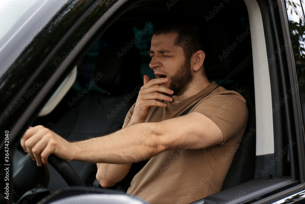 Tired man yawning while driving his modern car Tired man yawning while driving his modern car