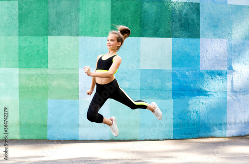 Fitness sport young girl in sportswear doing yoga fitness exercise on a wall background. Sporty gymnast child preteen running training outdoor.