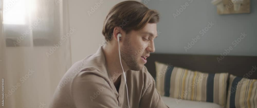 A young man speaking to someone through earphones while working on his laptop. Work from home concept. Slow motion, BMPCC 4K A young man speaking to someone through earphones while working on his laptop. Work from home concept. Slow motion, BMPCC 4K