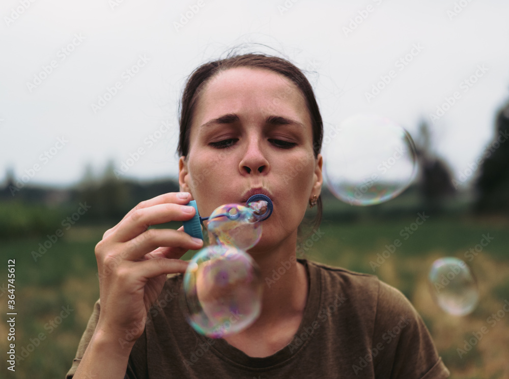 The girl blows soap bubbles. A young woman sits in nature and blows soap balls. The person in front. The girl blows soap bubbles. A young woman sits in nature and blows soap balls. The person in front.