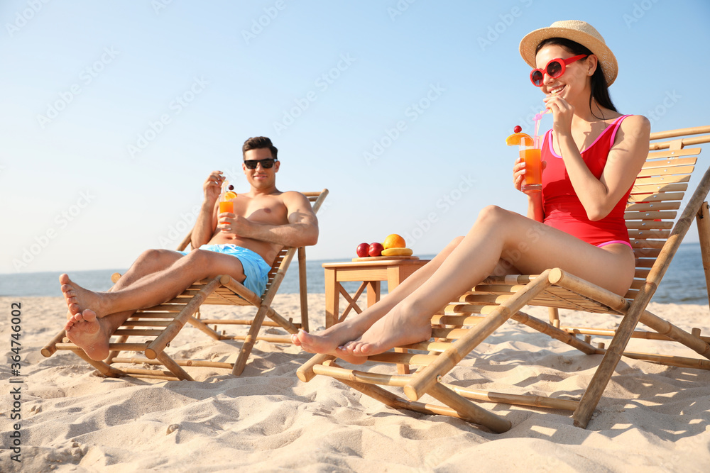 Couple with drinks resting on sunny beach at resort