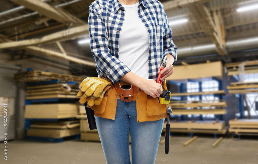 Fototapeta premium repair, construction and building concept - female worker with pliers and working tools on belt over workshop at woodworking factory background