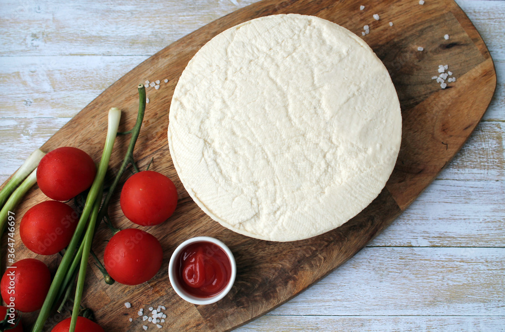 Homemade cheese made from goat's milk, small tomatoes on a branch, red sauce lie on a wooden Board on a wooden background. The concept of cooking delicious and healthy food Homemade cheese made from goat's milk, small tomatoes on a branch, red sauce lie on a wooden Board on a wooden background. The concept of cooking delicious and healthy food
