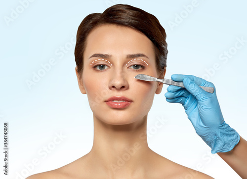 plastic surgery  blepharoplasty and beauty concept - beautiful young woman and hand with scalpel over blue background