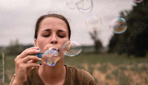 The girl blows soap bubbles. A young woman sits in nature and blows soap balls. The person in front.