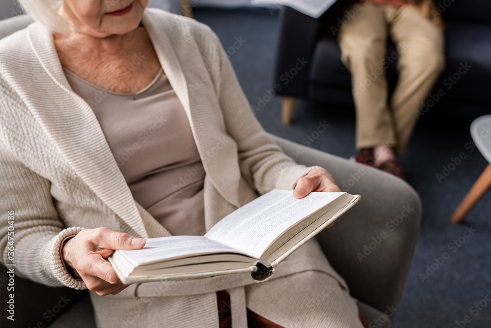cropped view of senior woman reading book near husband, selective focus cropped view of senior woman reading book near husband, selective focus
