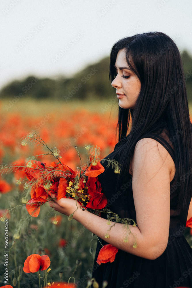 Naklejka premium Girl with long black hair in a black dress in a poppy field