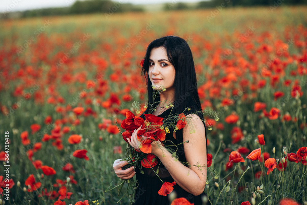 Girl with long black hair in a black dress in a poppy field Girl with long black hair in a black dress in a poppy field