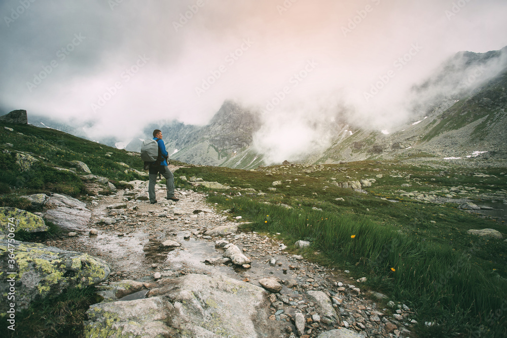 Man stands on trail in mountains. High peaks of mountains in the fog.