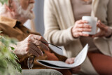 cropped view of senior man holding eyeglasses and newspaper near wife with cup of tea, selective focus