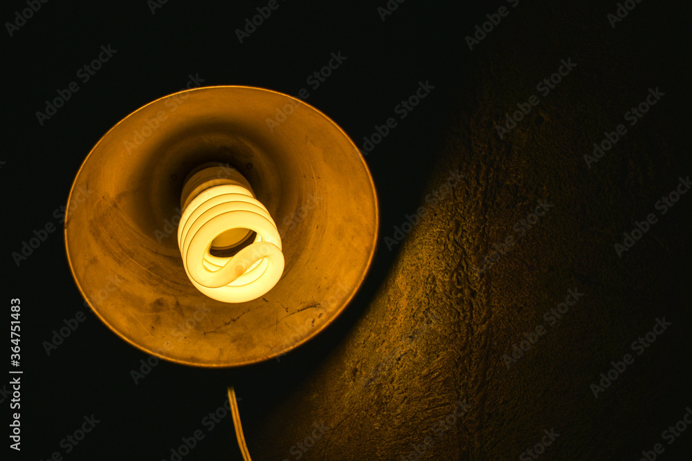 Large energy-saving light bulb in a dark room with concrete walls. close-up of a white spiral fluorescent light bulb in a dark room Large energy-saving light bulb in a dark room with concrete walls. close-up of a white spiral fluorescent light bulb in a dark room