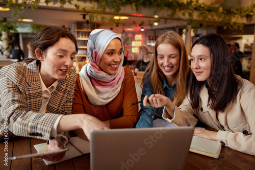 Women. Friends Meeting In Cafe. Four Smiling Girls Sitting In Restaurant With Laptop And Tablet. Diversity Female Working At Bistro. Freelance As Lifestyle. 