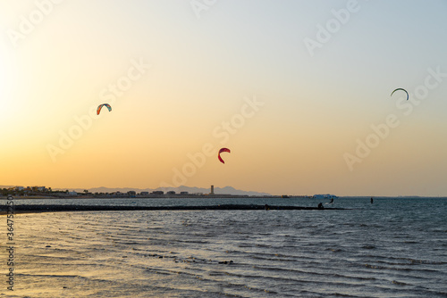 Kiters gliding over the Red sea surface. Extreme outdoor sport/activity/recreation. People in sport equipment riding on the water surface. Stunning marine scene. Beautiful sunset background.