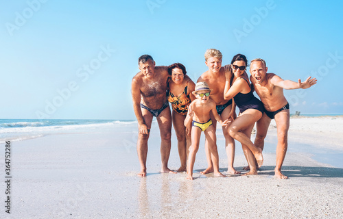 Three family generations on the one long shoot posing for group photo on the beach. Kids, teenagers, Parents and Grandparents together traveling concept image.