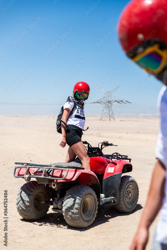 Obraz premium Young woman in safari trip through Egyptian desert driving Quad/ATV. Quad/ATV safari trip in the desert near Hurghada, Egypt.