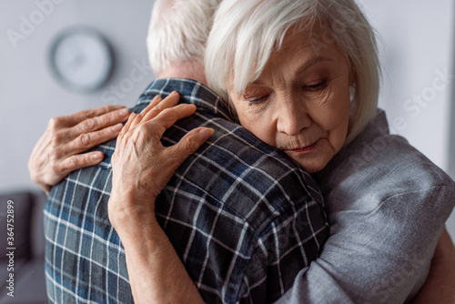 senior woman with closed eyes embracing husband sick on dementia