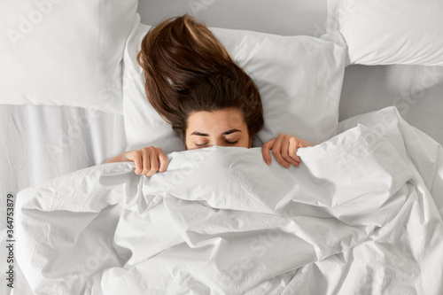 people, bedtime and rest concept - woman lying in bed under white blanket or duvet