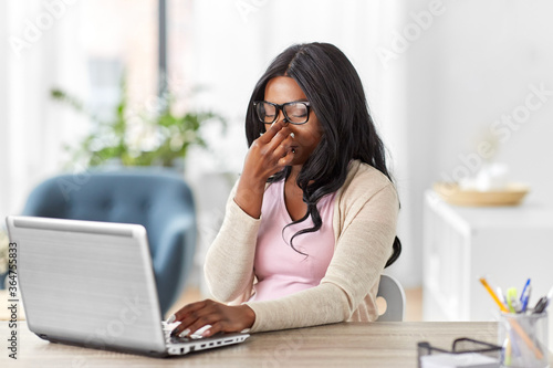 remote job, technology and e-learning concept - tired young african american woman in glasses with laptop computer working at home office and rubbing nose bridge