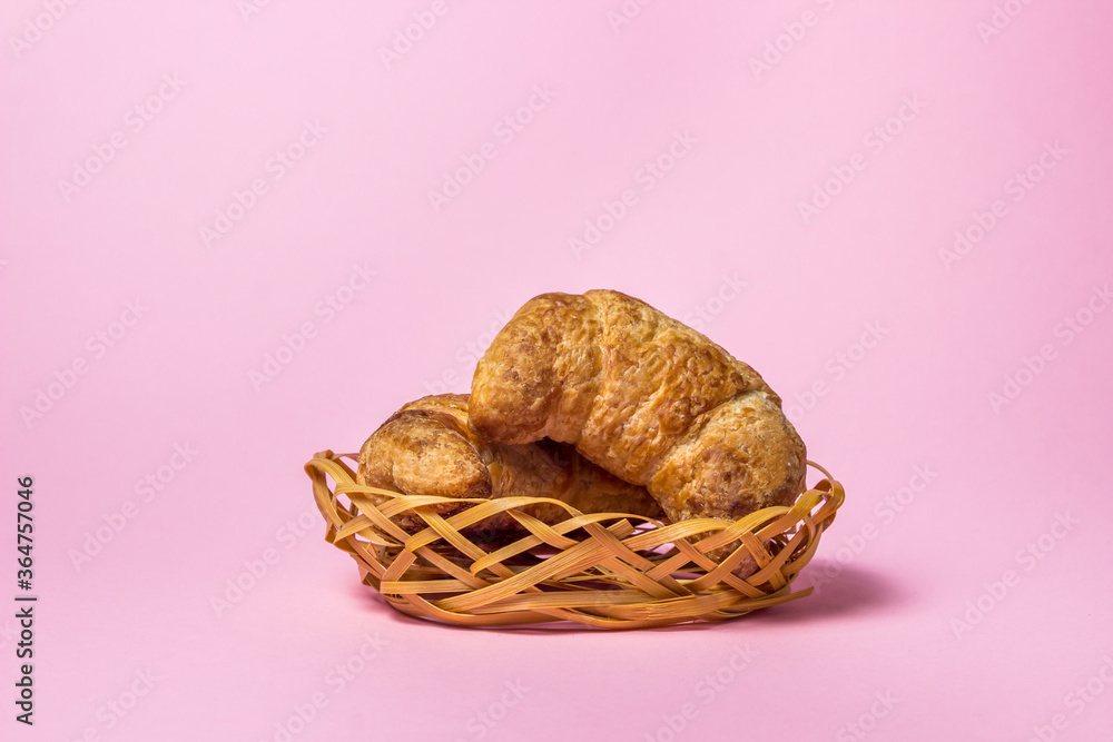 Croissants on a pink background. Two croissants lie in a small wicker basket