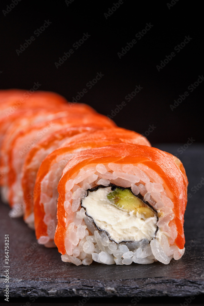 Beautiful sushi roll topped with salmon stuffed with cream cheese on a black stone board. Beautiful sushi roll topped with salmon stuffed with cream cheese on a black stone board.