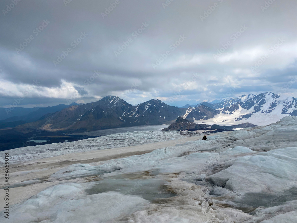 A climber with a backpack and trekking poles walks along a snowy ice trail. A climber with a backpack and trekking poles walks along a snowy ice trail.