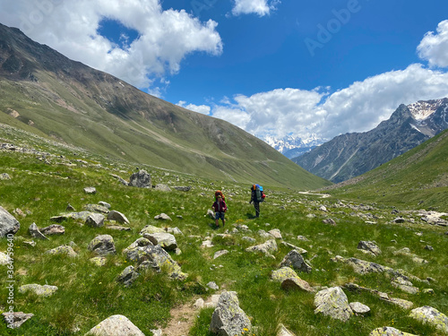 Green slopes of the northern Elbrus region. Two climbers are walking along a mountain trail.