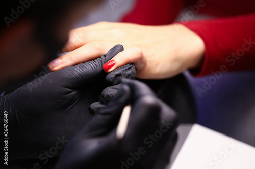 Close-up of professional nail master covering clients nails in red colour. Trendy season colour. Beautician appointment. Fresh manicure and salon treatment concept