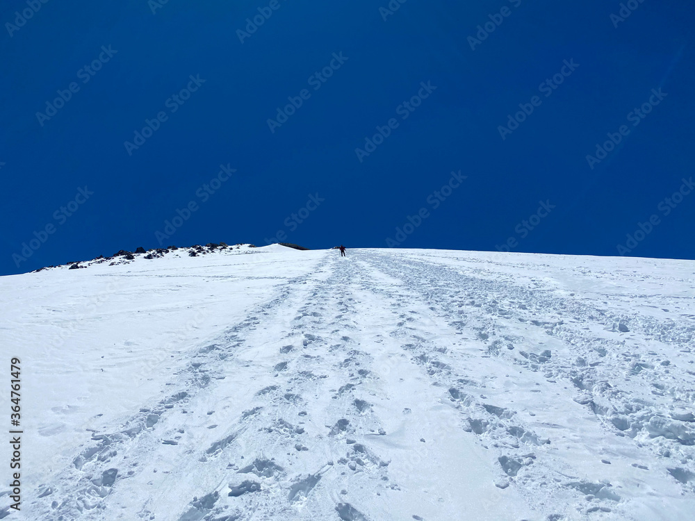 Mountain Elbrus. A climber with backpacks and trekking poles walks along a snowy path.