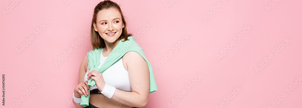 horizontal image of attractive overweight girl with sweatshirt over shoulders smiling while looking away on pink horizontal image of attractive overweight girl with sweatshirt over shoulders smiling while looking away on pink