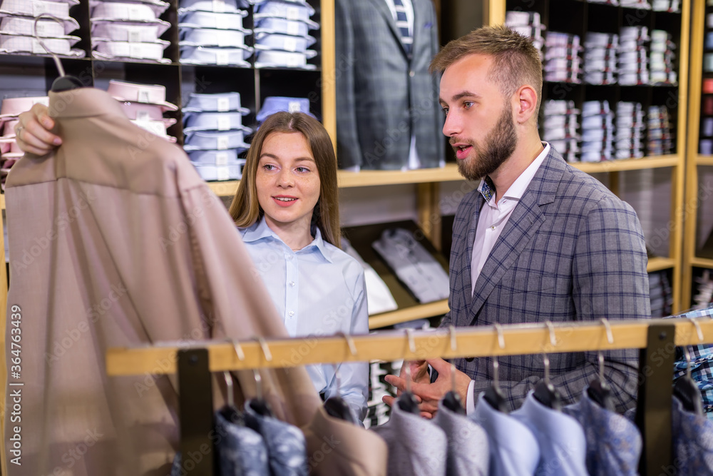 Obraz premium Successful young businessman looks at jacket, consulting with consultant in store.