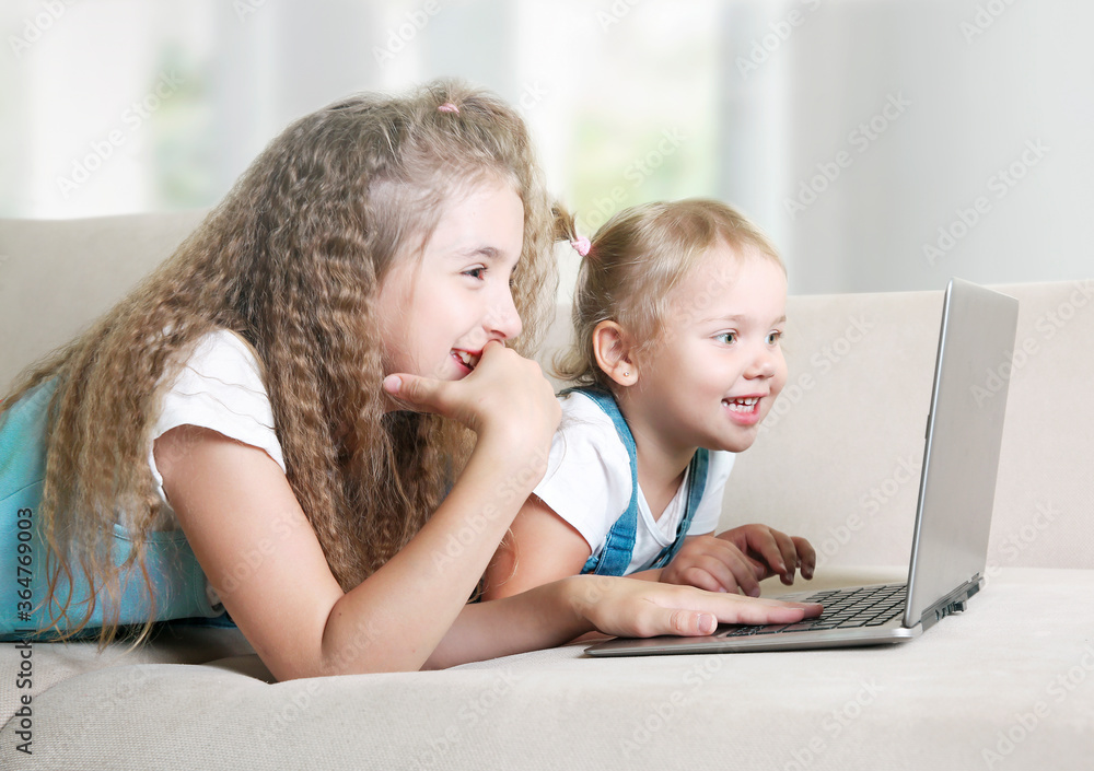 Children use laptop.Kids watching internet video.Little girls lying on sofa home and looking at notebook screen. Children use laptop.Kids watching internet video.Little girls lying on sofa home and looking at notebook screen.