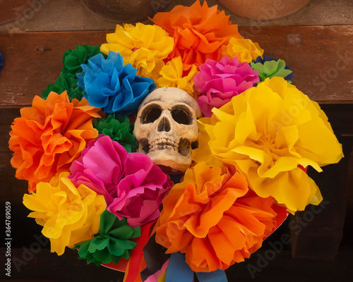 Fototapeta Naklejka Na Ścianę i Meble -  Fake human skull used as Halloween or Día de Muertos decoration. Multi-colored paper flowers. Day of the Dead decor. 