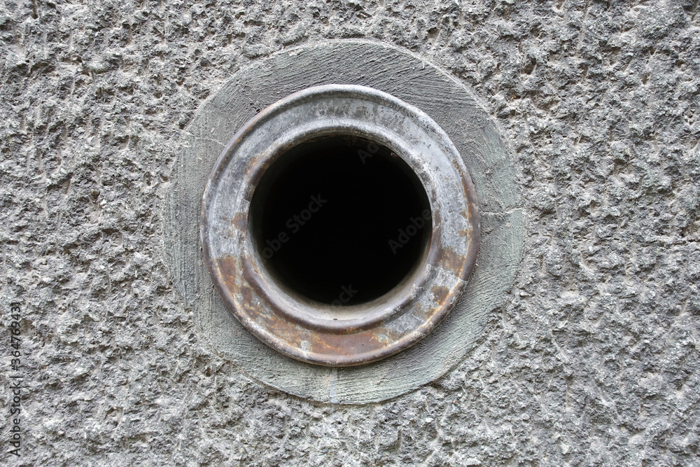 Peace of concrete rough wall with black hole in middle. Texture of grey rustic wall and metal rusty ring with hole.