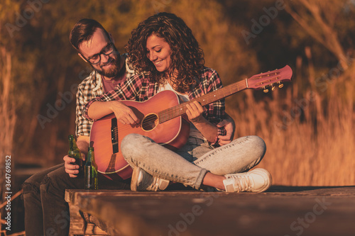 Couple playing the guitar and drinking beer at lake docks © Impact Photography