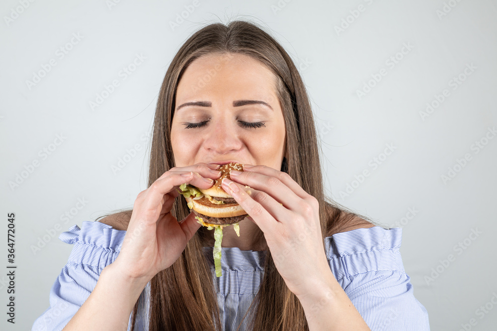 Portrait of a beautiful young woman eating a burger, isolated on white background Portrait of a beautiful young woman eating a burger, isolated on white background