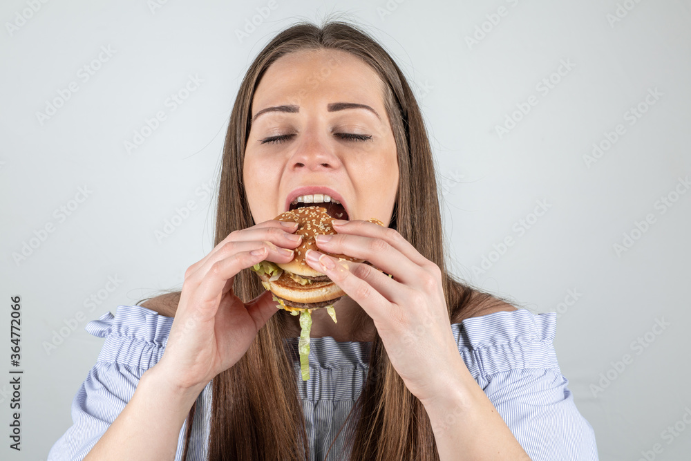 Portrait of a beautiful young woman eating a burger, close up, eyes closed, isolated on white background Portrait of a beautiful young woman eating a burger, close up, eyes closed, isolated on white background