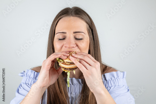Portrait of a beautiful young woman eating a burger  isolated on white background