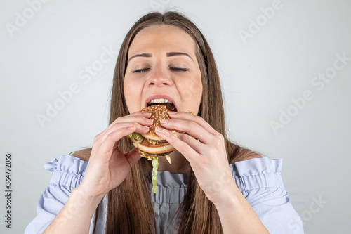 Portrait of a beautiful young woman eating a burger  close up  eyes closed  isolated on white background