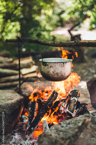 The pot is burning near the tent in the forest at night. Beautiful campfire in a tourist camp in the wild.
