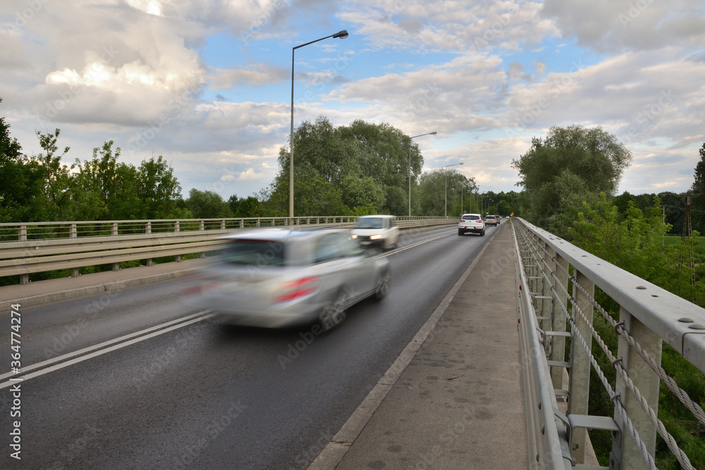 Blurry silhouettes of cars on the bridge against the background of clouds in the blue sky. Blurry silhouettes of cars on the bridge against the background of clouds in the blue sky.