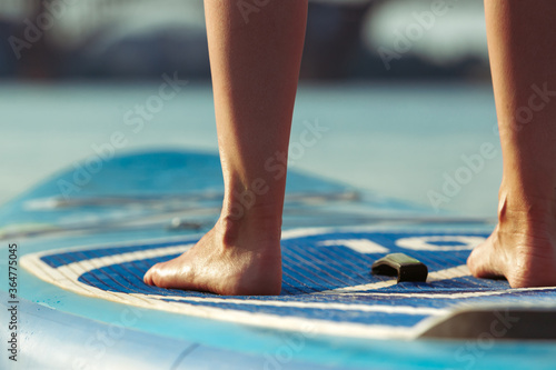 Close up legs. Young attractive woman standing on paddle board, SUP. Active life, sport, leisure activity concept. Caucasian woman on travel board in summers evening time. Vacation, resort, enjoyment.