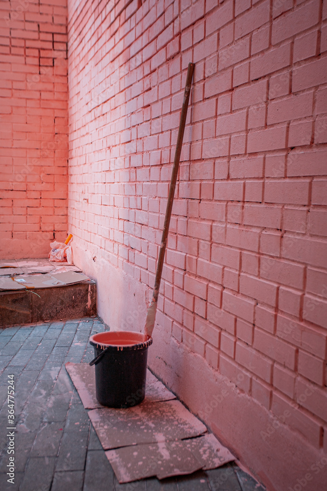 Pink brick wall. Paint roller for painting walls. Black bucket with paint. Repairs. High quality photo Pink brick wall. Paint roller for painting walls. Black bucket with paint. Repairs. High quality photo