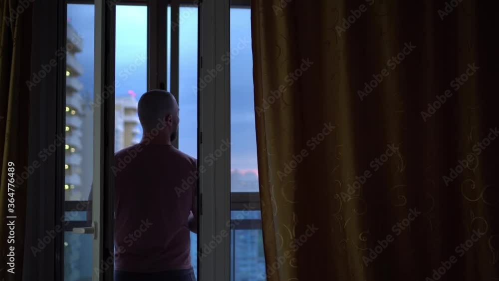 A Bald Man Stands Near the Open Window and Looks at The city. Outside the Multi-storey Building. The Concept of Freedom and Pleasure. Man Enjoys The View From The Window. A Bald Man Stands Near the Open Window and Looks at The city. Outside the Multi-storey Building. The Concept of Freedom and Pleasure. Man Enjoys The View From The Window.