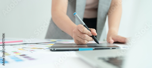 Young creative designer working at office. Graphic designer at work. Color swatch samples.Young female designer using graphics laptop while working with computer. 