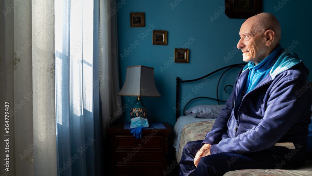 Fototapeta premium Covid-19 Profile view of an old man sitting on his bed looking sad at the window